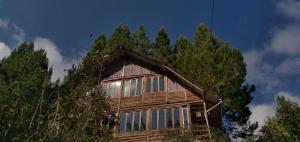 a wooden house with windows and trees in the background at La Casita de Oxapampa in Oxapampa