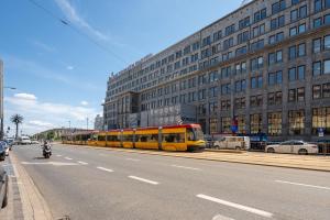 un tren amarillo en una calle de la ciudad con un edificio en JESS INN Hostel Rondo Charles de Gaulle, en Varsovia