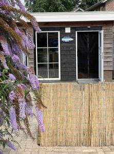 een huis met een hek en paarse bloemen bij Beach House met badkamer, boxspring & airco in Schoonebeek