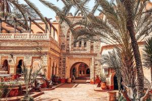 a large building with palm trees in a courtyard at Hebergement Tamazight 2 in Tarrast