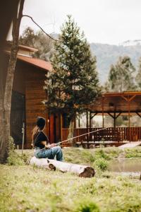 a girl sitting on a log in front of a cabin at Chalé Harmonia da Floresta- Pousada Cachoeira da Neve in Urubici