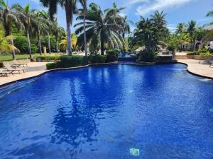 une grande piscine bleue bordée de palmiers dans l'établissement Beachfront Condo directly on the private beach - Ground Floor, à Six Huts