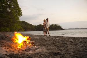 a couple standing next to a campfire on a beach at Santarena Hotel at Las Catalinas in Playa Flamingo