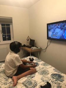 eine Person, die auf einem Bett sitzt und ein Videospiel spielt in der Unterkunft Croydon Near London in Shirley