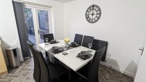 a dining room table with black chairs and a clock on the wall at ClariTurf - 4 Bedroom Semi - Private Parking near Turf Moor, Town Centre, Transport and Motorway Links next to Canal, 3 Parks and Lake - Sky and Netflix in Burnley