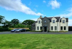 una gran casa blanca con coches aparcados en un aparcamiento en Boutique Country House Aldergrove, en Crumlin