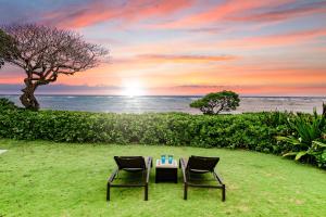 two chairs and a table in the grass with the sunset at OceanFront Kauai - Rhythm TVNC 4288 in Kapaa