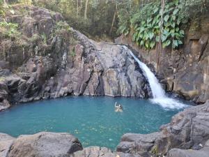 una persona che nuota in una piscina di fronte a una cascata di Charmant logement avec spa/petit-déjeuner inclus. a Pointe-Noire