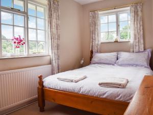 a bedroom with a bed with two windows at The Cottage in Blakeney
