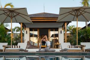a woman doing a yoga pose on the edge of a pool at EHOA BALI Nyanyi Boutique Hotel - In front of entrance to NUANU in Tanah Lot