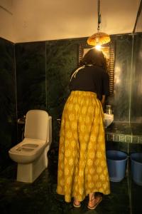 a woman in a yellow dress in a bathroom with a toilet at Open Road Hostel and Cafe in Jaisalmer