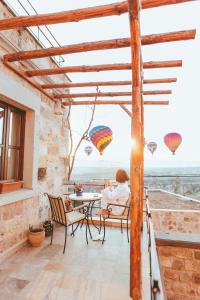 a woman sitting at a table on a patio with hot air balloons at Peristyle Cave Cappadocia- Special Class in Uchisar