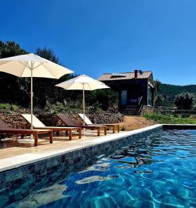 a swimming pool with two umbrellas and chairs and a house at Quinta das Levadas - Country House & Nature in Alvoco das Várzeas