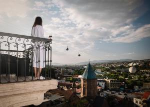 Eine Frau steht auf einem Balkon mit Blick auf eine Stadt in der Unterkunft Citadel Narikala Hotel in Tbilisi City