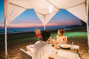 a man and woman sitting at a table on the beach at Chaolao Tosang Beach Hotel in Chao Lao Beach
