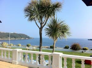 a white fence with two palm trees and the ocean at Escape to Ancarva Cottage near Falmouth in Perranwell