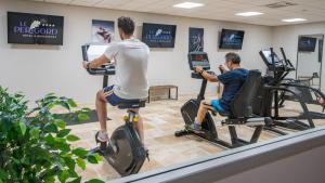 two men riding on exercise bikes in a gym at Hotel Le Perigord in La Roque-Gageac
