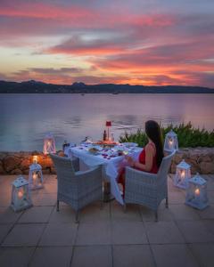 Una donna seduta a un tavolo di fronte all'acqua di Hotel La Rocca Resort & Spa a Baja Sardinia