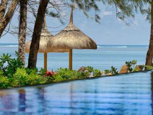 una piscina con sombrilla de paja y el océano en SO/ Sofitel Mauritius en Bel Ombre
