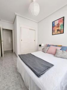 Un dormitorio con una gran cama blanca con una manta. en TorreSol Apartment, en Torrevieja