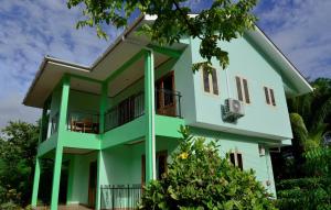una casa verde y blanca con un árbol en Chez Antoine Apartments, en Grand Anse