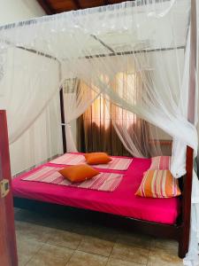 a bedroom with a canopy bed with pink sheets and orange pillows at White Villa in Unawatuna