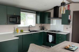 a green kitchen with green cabinets and a sink at Riverwood Lodge, The Boulevard, Seal Bay, Selsey in Selsey