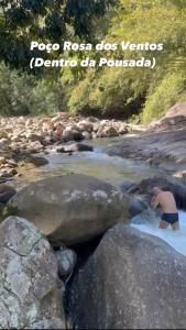 a man in the water in a river with rocks at Pousada Rosa dos Ventos Kchu in Cachoeiras de Macacu