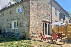 a house with two chairs and a table and an umbrella at Grange Labarthessié in Briatexte