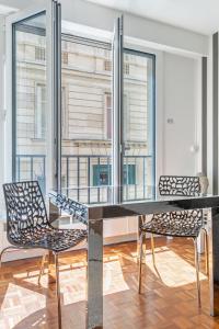 uma mesa de vidro e duas cadeiras num quarto com janelas em La Suite d'Avenue Foche em Paris