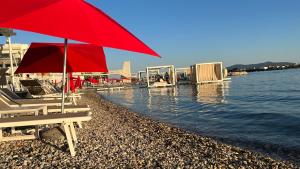 a beach with a red umbrella and chairs and the water at Apartments & rooms Ana Sukosan in Sukošan