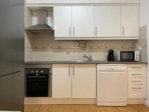 cocina con armarios blancos, fregadero y microondas en Apartamentos Castelos da Rocha, en Portimão