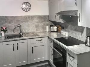 a kitchen with white cabinets and a sink and a clock at Pen Y Bont in Rhuddlan