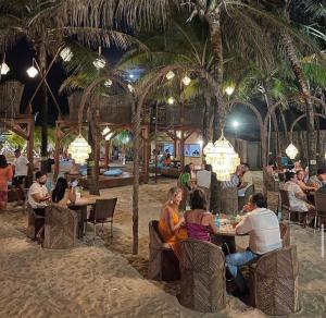 Happy Living Resort في فورتاليزا: مجموعة من الناس يجلسون على الطاولات على الشاطئ