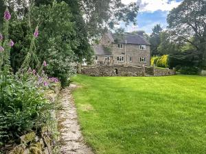 an old stone house with a green lawn and flowers at Mill Lea Cottage in Onecote