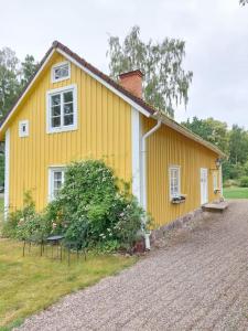 a yellow house with a gravel driveway in front of it at Trevligt eget hus med kakelugn i lantlig miljö in Vikingstad