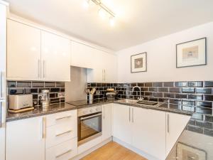 a kitchen with white cabinets and black tiles on the wall at Raven Cottage in Barnard Castle