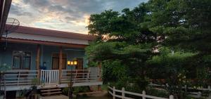een blauw huis met een witte veranda en een boom bij โฮมสเตย์ ยายหนั่น in Ban Nong Kham Tai