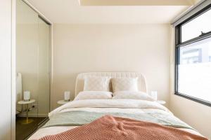 a white bedroom with a large bed and a window at Beachside flat with free parking in Melbourne