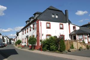 a white building with a black roof on a street at Hotel & Restaurant Hüllen in Barweiler