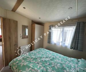 a bedroom with a bed with a green comforter and a window at Homely 2 bed @ Seal Bay Resort in Selsey