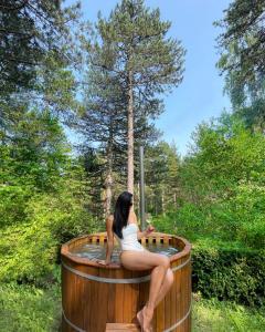a woman sitting in a hot tub in the woods at National Park Sauna Retreats - Villa 68 Pines in Kaludjerske Bare