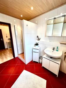 uma casa de banho com um lavatório branco e um piso vermelho em Ferienwohnung Sattler em Mistelgau