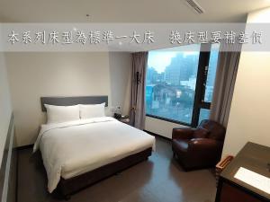 um quarto com uma cama, uma cadeira e uma janela em Hotel J Taoyuan em Pingzhen