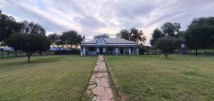 a large white house in a field with trees at Karoo Leeu Self Catering in Oudtshoorn