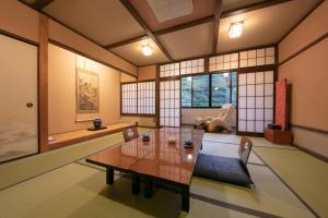 ein Wohnzimmer mit einem Tisch, Stühlen und Fenstern in der Unterkunft Yumoto Ueyama Ryokan in Himeji