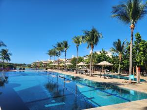 ein Swimmingpool mit Palmen und Sonnenschirmen in der Unterkunft Apto Completo l Excelente Vista em Golf Ville Resort in Aquiraz