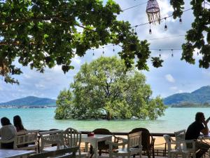 a group of people sitting at tables in front of a body of water at Baan Panwa Resort in Panwa Beach