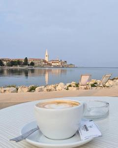 a cup of coffee sitting on a table near the water at Apartmani Karmen Mali Maj in Poreč
