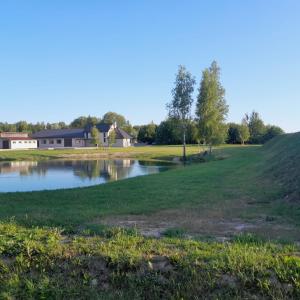 a pond in a field with a house in the background at Jaunvaltes in Ragana